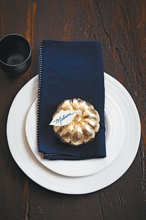a modern Thanksgiving place setting with white plates, a navy napkin and a gilded pumpkin is a cool and fresh idea