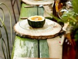 a rustic fall or Thanksgiving tablescape with a green table, wood slices as placemats, greenery and dark glass bottles is very cozy