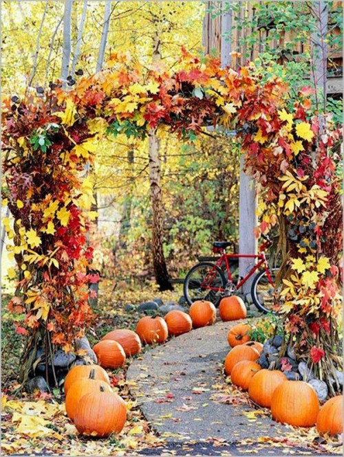 a super lush Thanksgiving and fall wedding arch fully covered with bright fall leaves and greenery and with pumpkins lining up the aisle is amazing