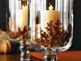 large glasses filled with fall leaves and with candles inside are gorgeous for rocking them at a fall wedding, this is a simple and lovely idea