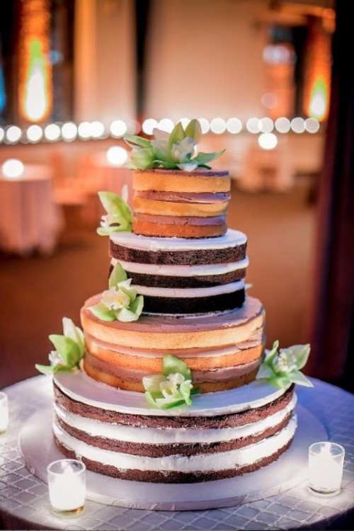 a naked wedding cake with usual and chocolate tiers, with lots of frosting and green flowers and candles around is a stylish idea for a summer wedding