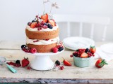 a naked wedding cake with frosting, with fresh berries, and little flag cake toppers is a delicious and sumptuous idea for a summer wedding