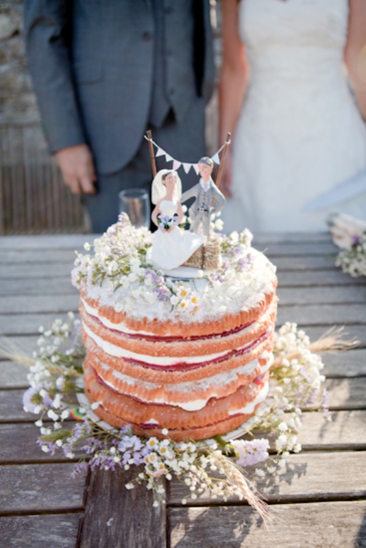 a relaxed summer naked wedding cake with frosting, some white and lilac blooms and couple and bunting cake toppers is a gorgeous idea for a relaxed summer wedding