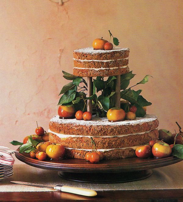 a two tier naked wedding cake with greenery and caramel and chocolate dipped apples and fruit is a creative idea
