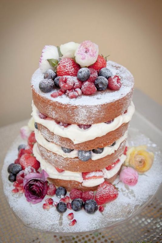 a naked wedding cake with frosting and fresh berries, sugar powder is a lovely idea for a summer wedding
