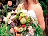 an oversized wedding bouquet that includes pink and burgundy blooms, oversized pinecones, apples, berries, king proteas, crystals and lots of greenery