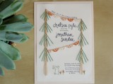 a neutral wedding invitation with black calligraphy, with embroidered trees, buntings, flowers and a dino is a fun idea
