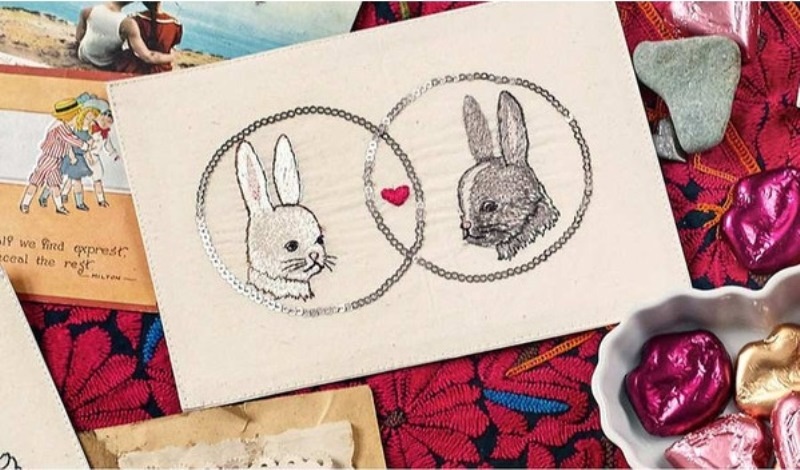 a neutral wedding invitation with embroidered bunnies and a heart in the center is a lovely idea for a cozy wedding