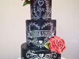 a black chalkboard wedding cake with lovely chalk decor, with coral faux blooms and greenery for a relaxed or rustic wedding