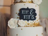 a white wedding cake with gold polka dots, a chalkboard sign with chalking, white sugar blooms is a lovely idea for a modern wedding