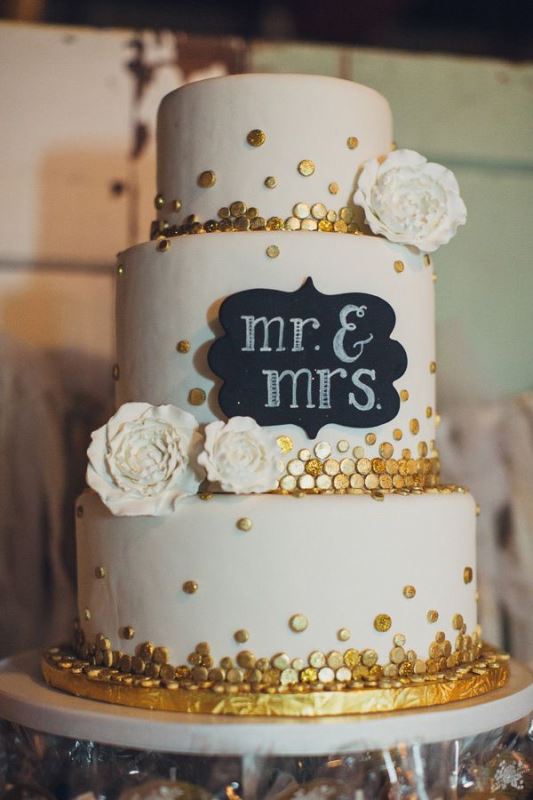 A white wedding cake with gold polka dots, a chalkboard sign with chalking, white sugar blooms is a lovely idea for a modern wedding