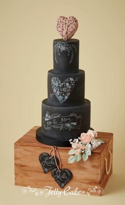 a black chalkboard wedding cake with beautiful chalk inspired decor and a pink yarn heart on top is a unique idea