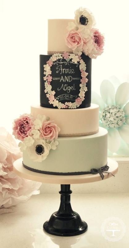 a creative wedding cake with white, an aqua, a black chalkboard tier with chalking and some fresh pink and white blooms plus a floral wreath on the chalkboard