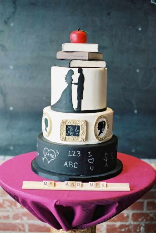 a unique wedding cake with white and black chalkboard tiers, with silhouettes, mini artworks and chalking, some sugar books and an apple on top is jaw-dropping
