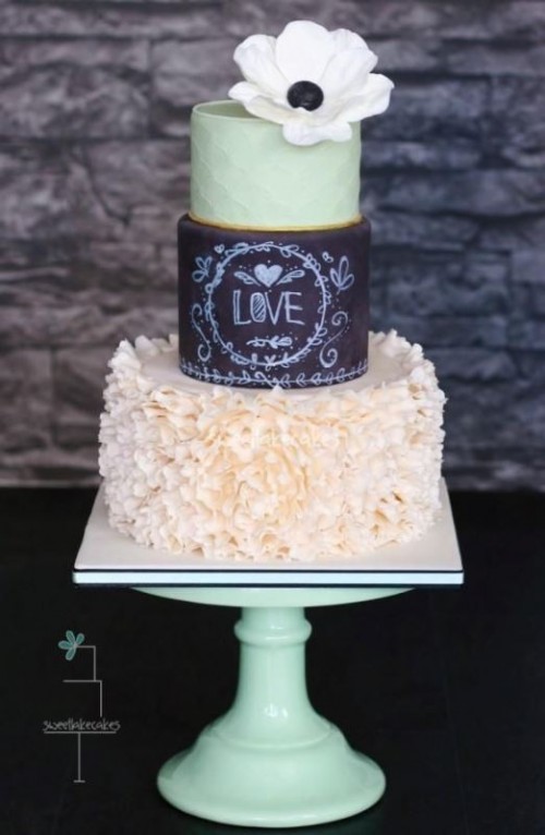a unique wedding cake with a neutral ruffle tier, a chalkboard one with chalking, a light gree tier with a white bloom on top is a gorgeous idea for a modern wedding