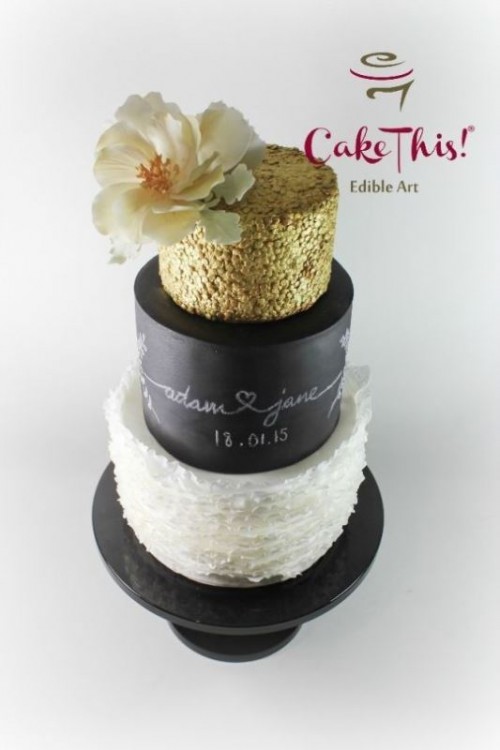 a lovely wedding cake with black chalkboard tiers, a white ruffle one and a gold glitter tier on top, with a white sugar flower on top