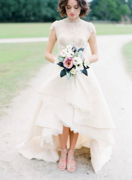 a romantic vintage-inspired lace high low wedding dress with a layered skirt, a high neckline and cap sleeves of an ivory shade is a lovely idea for a modern romantic bride