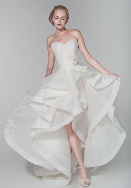 a romantic strapless wedding dress with a sweetheart neckline, a layered ruffle high low skirt with a train and a brooch on the bodice