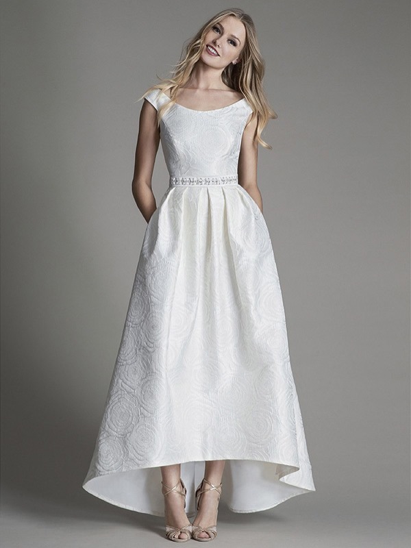 A simple modern A line lace high low wedding dress with a bateau neckline and cap sleeves, an embellished sash and chic gold shoes