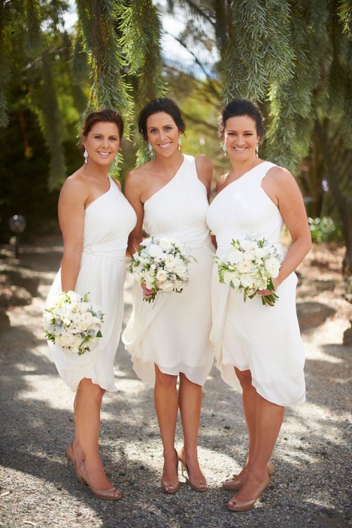 matching white one shoulder knee bridesmaid dresses with asymmetrical skirts are great for a modern tropical wedding