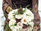 a white wedding bouquet with greenery and pinecones is a beautiful rustic solution for a winter wedding