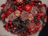 a gorgeous red winter wedding bouquet of pinecones, red berries, apples, large rhinestones covered with silver threads as if it’s frozen