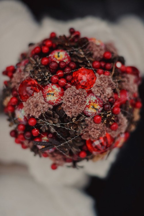 a gorgeous red winter wedding bouquet of pinecones, red berries, apples, large rhinestones covered with silver threads as if it's frozen