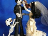 a scary and fun cake topper showing a skeleton couple eating wedding cake together and their skeleton dog is a lovely idea for a themed wedding