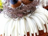 a bundt wedding cake with drip and faux bird cake topper in a nest, with feathers to remind of creating a couple’s own nest and showing that they are birds of feather