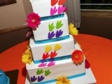 a colorful square wedding cake with bright gerberas and unique and fun marrying lizzard toppers is a very humorous idea