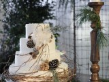a cozy rustic wedding cake in white, with branches, pinecones and foliage and faux blooms