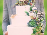 a pure white wedding cake topped with moss, succulents, faux mushrooms, a butterfly and even a faux nest on top