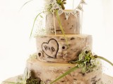 a woodland bark wedding cake with a carved heart, blooms and greenery and a banner topper
