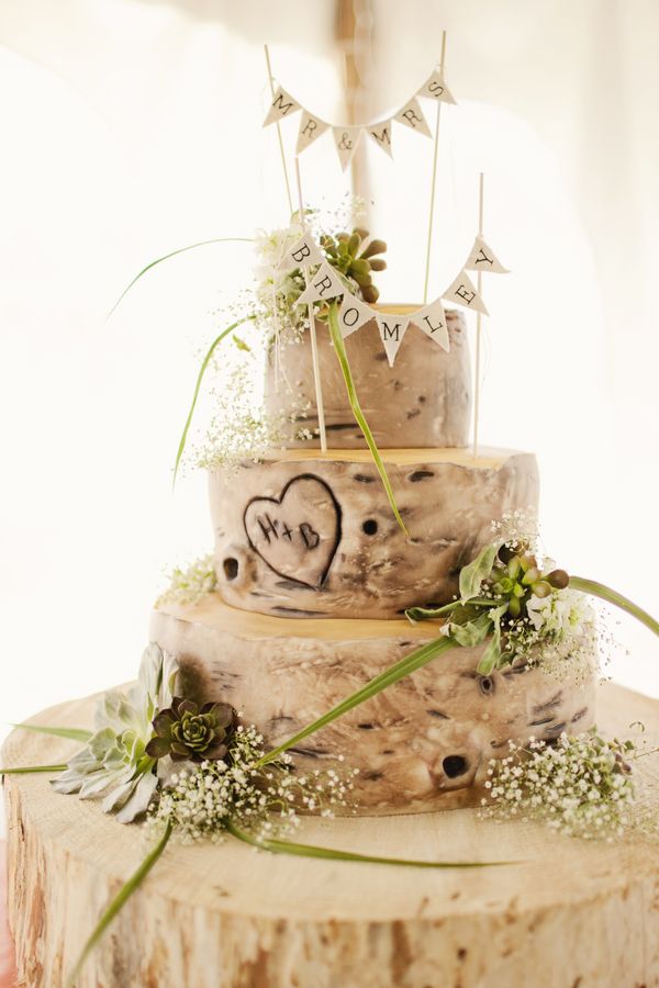 A woodland bark wedding cake with a carved heart, blooms and greenery and a banner topper