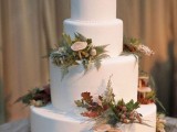 a pure white wedding cake topped with mushrooms, ferns, foliage and berries that are all edible