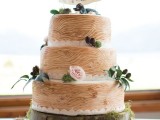 a woodland wedding cake that imitates wood, with fresh blooms and greenery and a bird topper with a banner