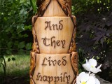a fantasy woodland wedding cake that seems to be carvedout of wood, with a fake burnt inscription and sugar blooms on top