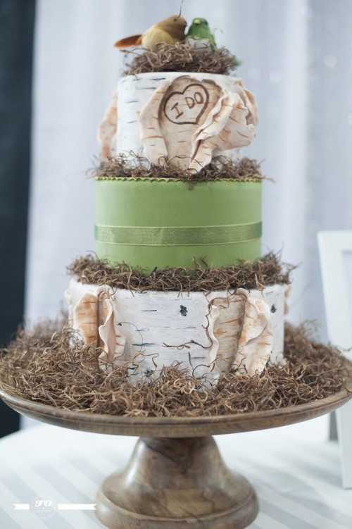 a woodland wedding cake in green and with bark, with hay, moss, a nest with birds topper