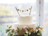 a white textural buttercream wedding cake topped with a banner, on a wood slice with greenery and blooms