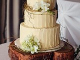 a rustic wedding cake with neutral textural buttercream, greenery, moss, white blooms and served on a wood slice