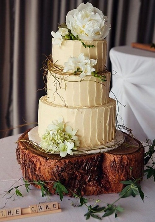 a rustic wedding cake with neutral textural buttercream, greenery, moss, white blooms and served on a wood slice