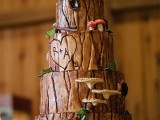 a woodland wedding cake that seems to be covered with tree bark, fake foliage and mushrooms plus owl toppers