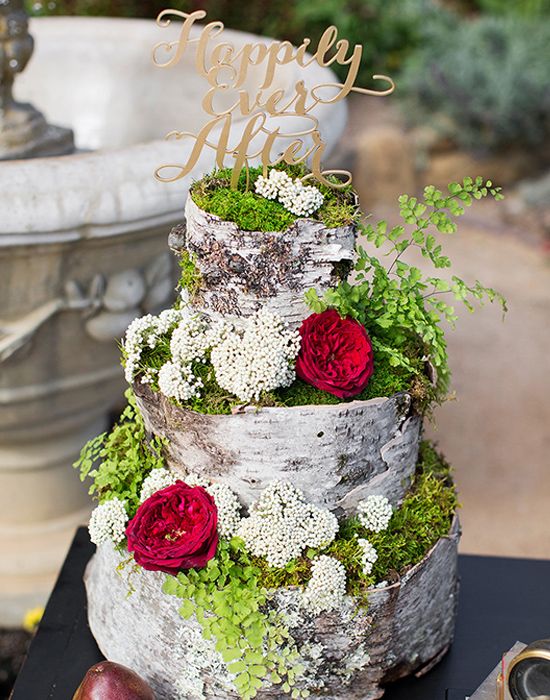 A unique woodland wedding cake that seems to be made of bark, moss and decorated with fresh blooms plus an elegant topper