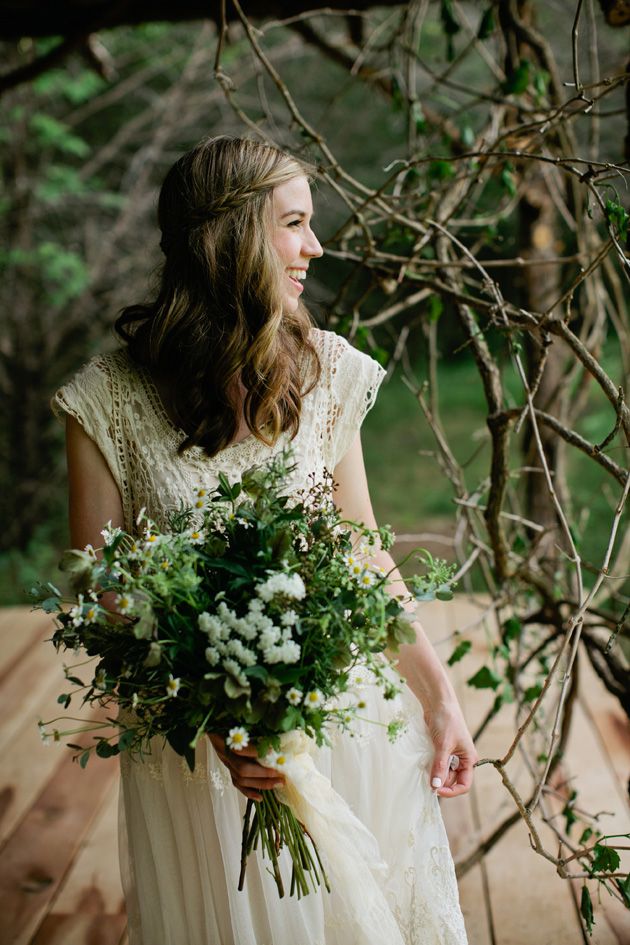 A relaxed boho lace cap sleeve wedding dress with a scoop neckline and a bouquet of wildflowers