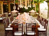 a vineyard wedding reception with a table with white linens, pink blooms and jars with lights hanging over the table is a welcoming space