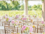a chic vineyard wedding reception space with greenery views and greenery hanging down from the chandeliers, neutral tablescapes with pink blooms is amazing