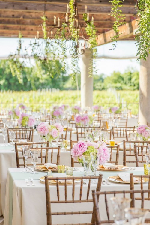 a chic vineyard wedding reception space with greenery views and greenery hanging down from the chandeliers, neutral tablescapes with pink blooms is amazing