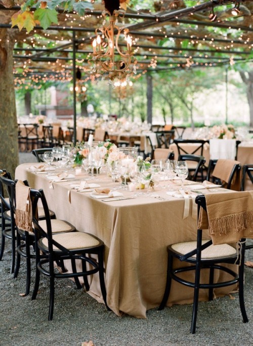 a cozy neutral wedding reception with tan and beige linens, neutral blooms, crystal chandeliers and beige chair covers for a perfect match