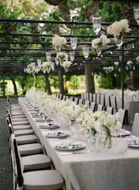 a white vineyard wedding reception with white blooms in glasses hanging down, neutral linens and white blooms on the table looks very sophisticated