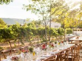 a relaxed vineyard wedding reception with a kraft paper runner, bright and white blooms and greenery, rustic chairs and tables
